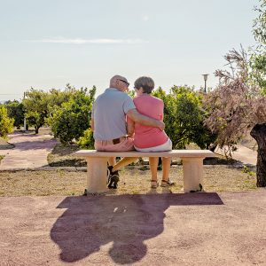 Et eldre ektepar som sitter på en benk og holder rundt hverandre.